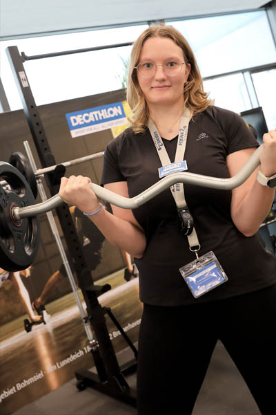 Eine Frau hält eine schwere Hantel und blickt in die Kamera.